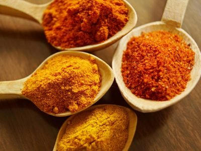 Close-up of vibrant spices like turmeric and chili powder in wooden spoons.