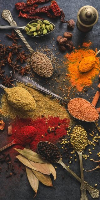 Vibrant array of spices including turmeric, cumin, and chili arranged on a dark surface.