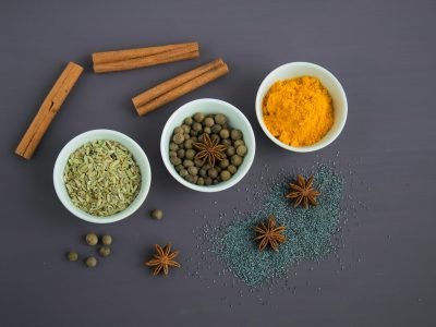 Flat lay of assorted spices including cinnamon, turmeric, and star anise on a dark surface.